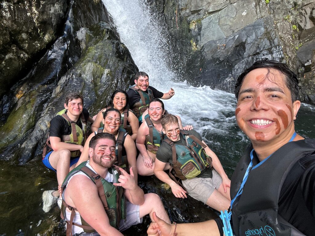 Group of happy tourists posing by a hidden waterfall during the El Yunque Rainforest tour in Puerto Rico, enjoying the natural beauty and adventure.