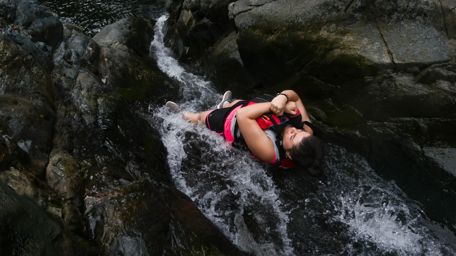 Guest riding a natural rock water slide into a freshwater pool on an El Yunque rainforest tour in Puerto Rico